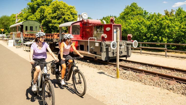 Deux cyclistes passent devant une vieille locomotive sur une piste cyclable.