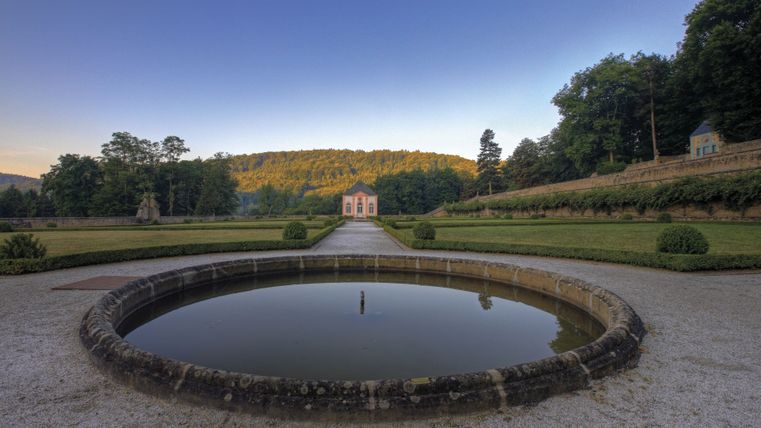 Garden pavilion of Weilerbach Castle with fountain in the foreground and trees in the background.