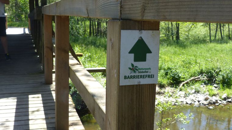 An accessibility sign attached to a covered wooden bridge over a river