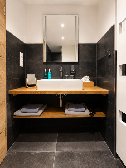 Een moderne badkamer met een grote spiegel en een elegante houten plank. Op de plank zijn hygiëneproducten en handdoeken netjes geplaatst.