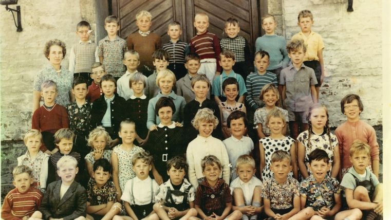 Un groupe d'enfants se tient devant une grande porte. Ils portent des vêtements de styles variés et sourient à la caméra.