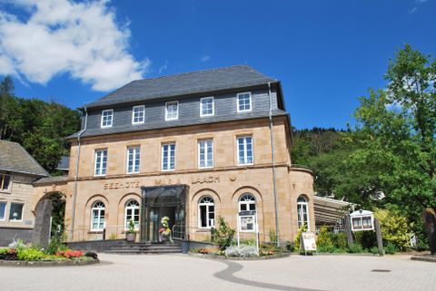 Un bâtiment historique avec une façade élégante et un ciel clair. Au premier plan, on peut voir des fleurs et des arbres.
