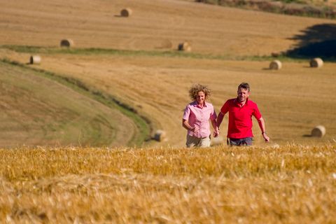 Een stel loopt hand in hand door een gouden veld met hooibalen op de achtergrond.