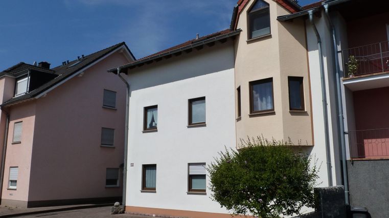Une maison moderne avec une façade lumineuse. À côté, se trouve un autre bâtiment en rose pâle.