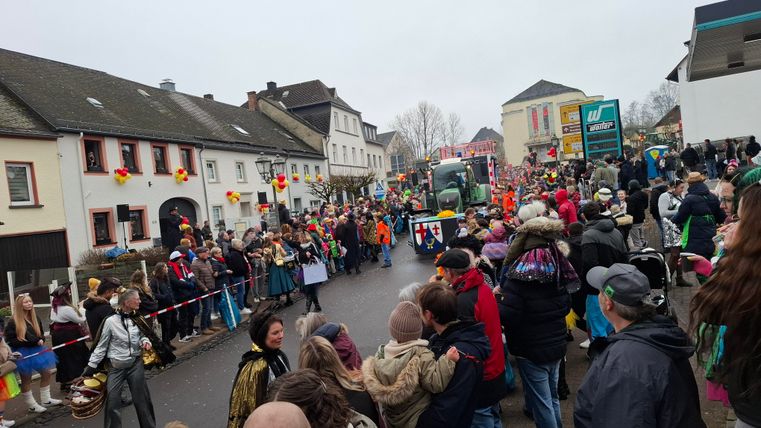 A colorful parade with many people on the street. There are festive costumes and decorated houses.