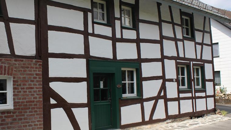 Een traditioneel vakwerkhuis met witte muren en bruine balken. De deur is groen en de vloer is met stenen verhard.