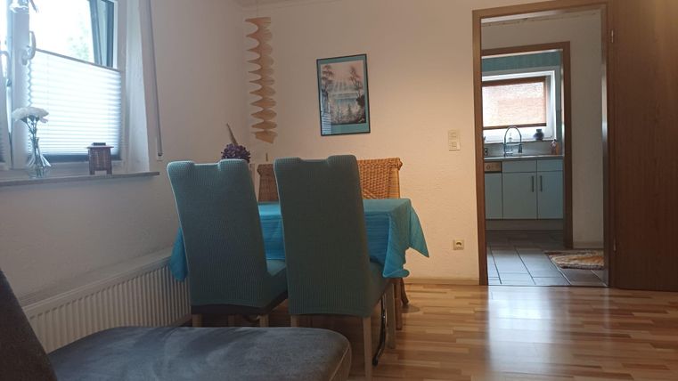 Une salle à manger accueillante avec une table et des chaises. À l'arrière-plan, la cuisine est visible.