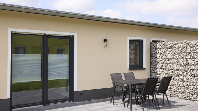 A modern residential building with a glass terrace door and a cozy outdoor seating area. A stone wall ensures privacy.