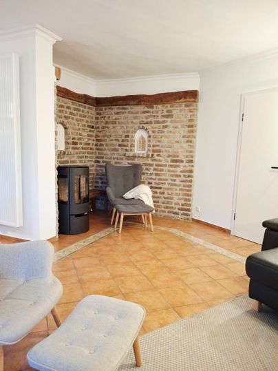 Ein gemütliches Wohnzimmer mit einer Backsteinwand und modernen Möbeln. Ein Kamin sorgt für eine warme Atmosphäre.