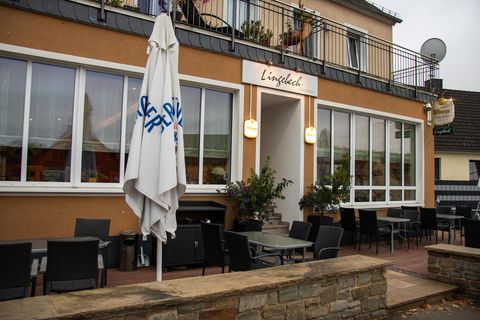 Een sfeervol restaurant met een terras en meerdere tafels. De façade is helder verlicht, en een parasol staat voor de ingang.