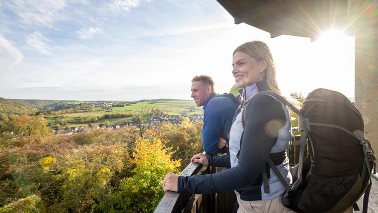 Ein Paar steht auf einem Balkon und betrachtet die wunderschöne Landschaft. Die Sonne scheint und die Umgebung ist mit herbstlichen Farben geschmückt.