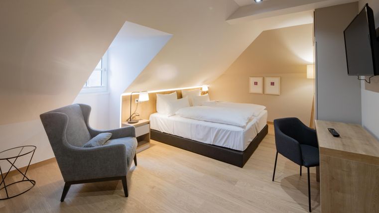 Een moderne slaapkamer met een groot bed en gezellige meubels. De muren zijn licht en de ruimte heeft een heldere, uitnodigende sfeer.