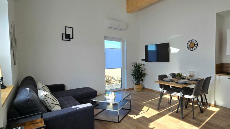 A modern living room with a black sofa and a dining table.
Large windows let in plenty of light and offer a view outside.