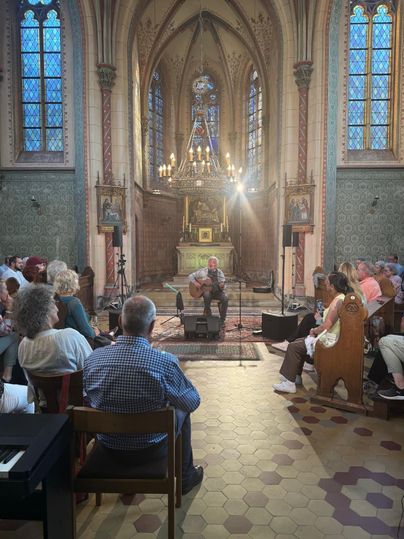 Ein Musiker spielt in einer Kirche für ein Publikum. Die Atmosphäre ist warm und einladend mit schönen Fenstern und historischer Architektur.