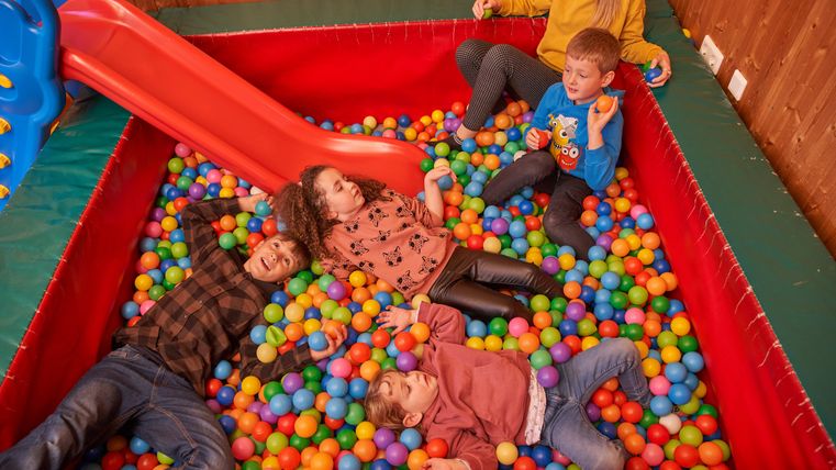 Kinderen spelen in een kleurrijk ballenbad met een glijbaan. Ze lachen en genieten van de tijd samen.