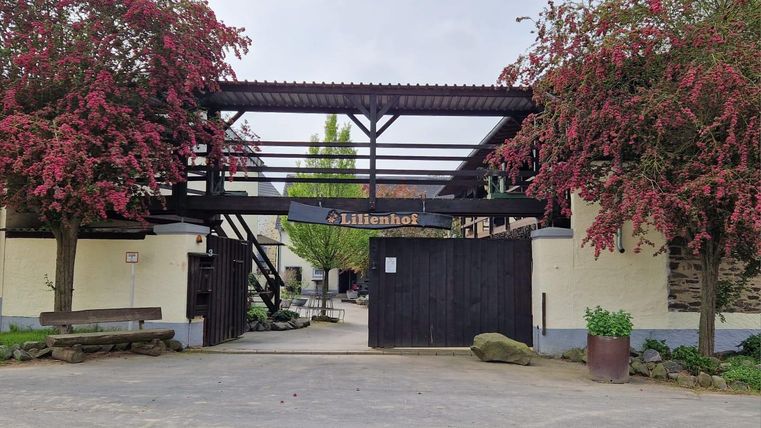 Une entrée vers une cour avec l'inscription "Liliensthof". Des fleurs colorées entourent l'entrée et créent une atmosphère accueillante.