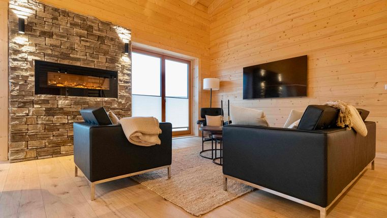 Ein modernes Wohnzimmer mit Holzwänden und einem Kamin aus Naturstein. Zwei schwarze Sofas und ein flauschiger Teppich schaffen eine einladende Atmosphäre.