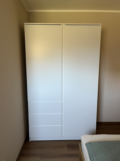 Une armoire blanche se trouve dans une pièce. Le sol est en bois et le style est moderne et minimaliste.