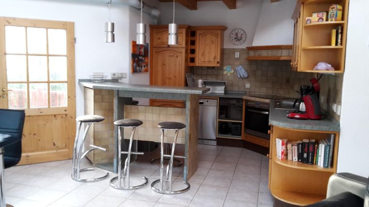 Une cuisine moderne avec des armoires en bois et un bar avec des tabourets. Le design est lumineux et accueillant, avec beaucoup d'espace pour les activités.