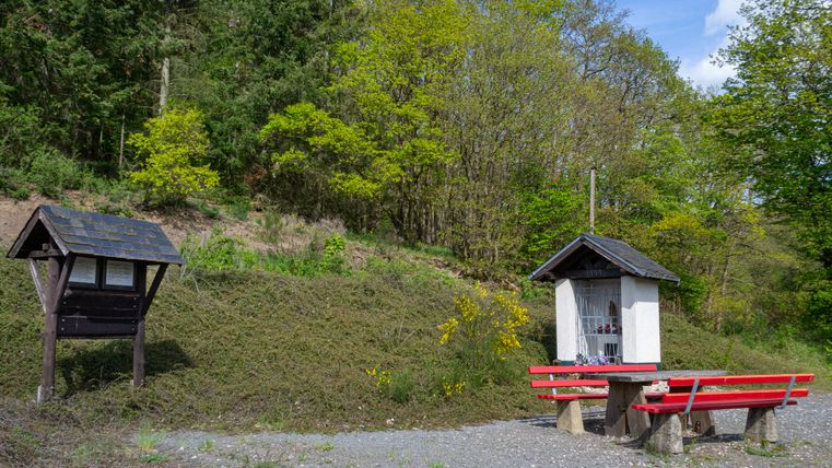 Aire de pique-nique avec banc rouge et petit sanctuaire dans la forêt.