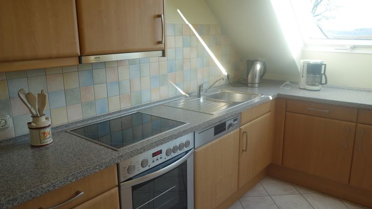 A modern kitchen with wooden cabinets and a bright tiled floor. The countertop is made of granite and there are various kitchen appliances.