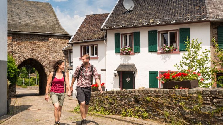 Un couple se promène dans l'enceinte historique du château de Reifferscheid, en passant devant des maisons à colombages et un arc de porte.