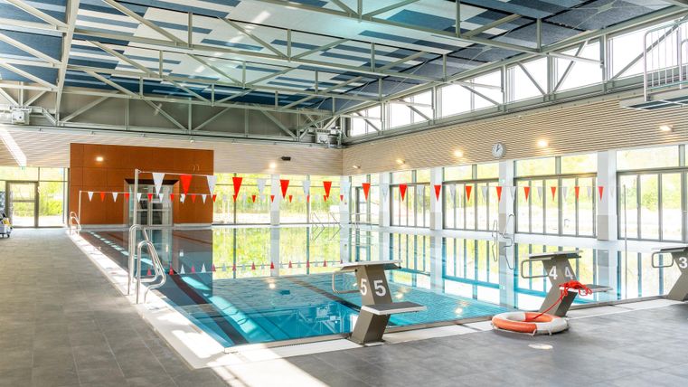 Une piscine couverte moderne avec une piscine bleue et de grandes fenêtres. L'environnement est lumineux et accueillant, avec des fanions colorés qui pendent au bord de la piscine.
