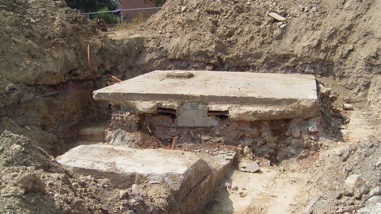 A excavated plot with a concrete foundation. Raised earth layers lie around the foundation.