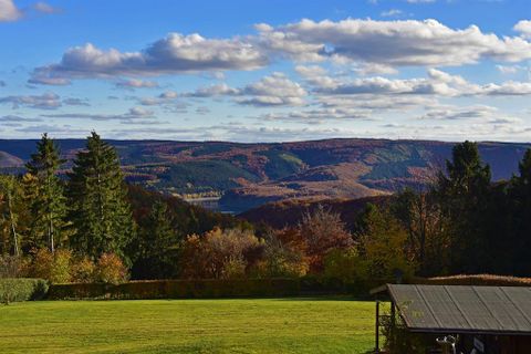 Eine malerische Landschaft mit bunten Herbstbäumen und sanften Hügeln. Der Himmel ist klar mit einigen Wolken und bietet einen schönen Blick auf die Natur.