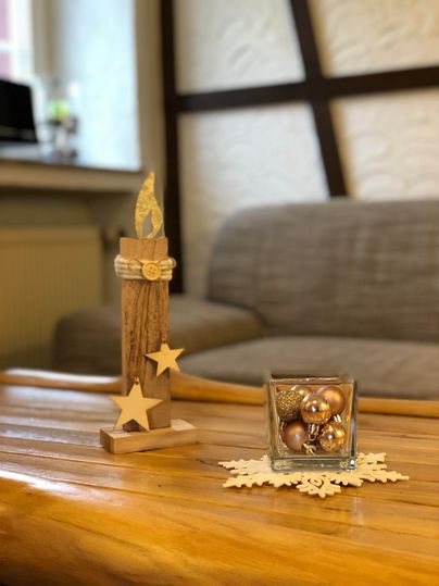 Een decoratieve tafel met een houten standaard en een kaars, versierd met sterren. Daarnaast staat een glazen emmer met gouden ballen op een mooie ondergrond.