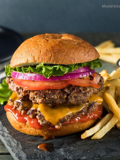Een sappige burger met twee rundvlees patties, cheddar kaas, verse sla, tomaten en uien. Daarnaast worden er knapperige frietjes op een zwarte steen geserveerd.