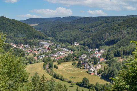 Blick auf ein Dorf in einem bewaldeten Tal mit Hügeln im Hintergrund.