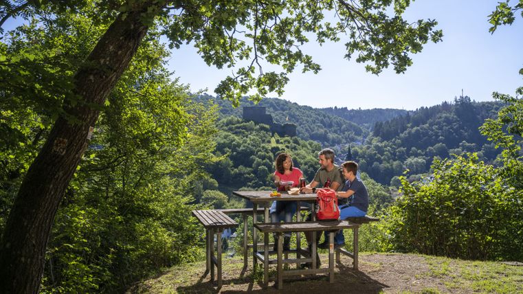 Three people sit at a picnic table in the countryside with a view of a ruined castle.
