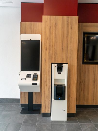 Un nouveau distributeur pour les commandes se trouve à côté d'un distributeur de boissons. Les murs sont décorés de panneaux en bois avec des accents rouges.