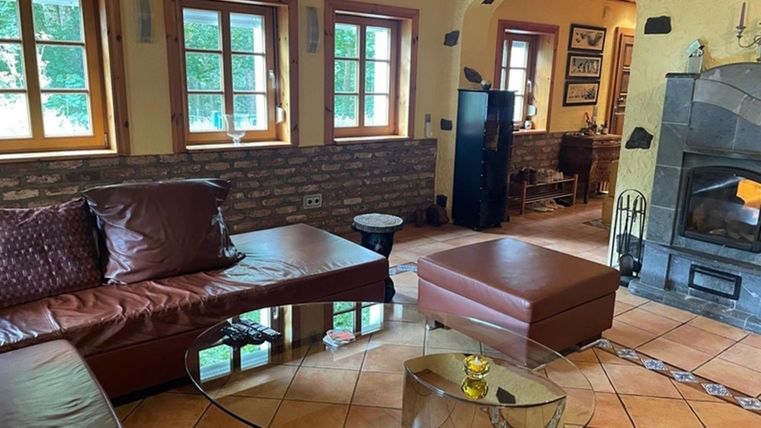 A cozy living room with an L-shaped leather couch and a round glass table. Large windows let in plenty of daylight, and the fireplace provides a warm atmosphere.