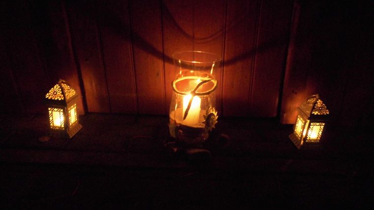 A calm and atmospheric scene with a burning candle in a glass and two glowing lanterns. The light creates a cozy atmosphere.