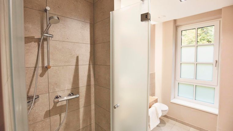 Moderne douche in een lichte badkamer met tegels en een raam. De ruimte oogt schoon en uitnodigend.