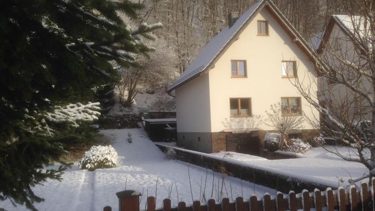 A quiet house in the snow, surrounded by a garden and a wooden fence. The landscape is wintery and peaceful.