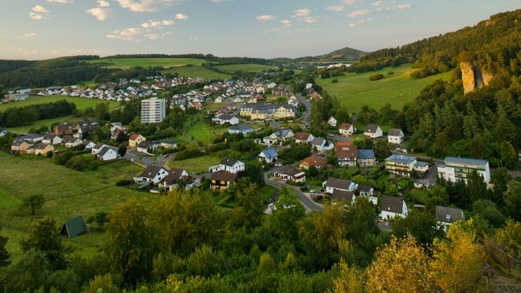 Panoramablick auf Gerolstein mit Häusern, Wiesen und bewaldeten Hügeln im Hintergrund.