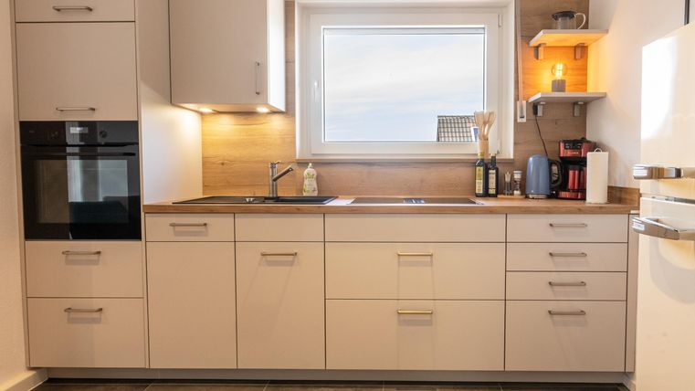 Een moderne keuken met witte kasten en een houtwerkblad. Het grote raam zorgt voor veel daglicht en een vriendelijke sfeer.