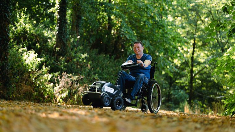 A man in a wheelchair with traction device, surrounded by leaves and trees