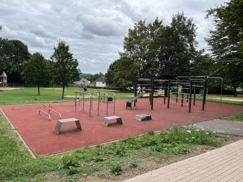 Een speelplaats met turntoestellen op antislipvloer. Op de achtergrond zijn groene bomen te zien en de lucht is bewolkt.