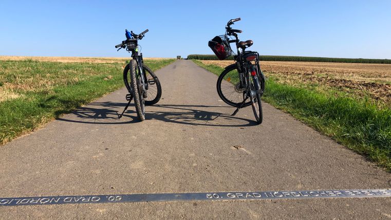 Twee fietsen staan geparkeerd op een pad dat de 50e breedtegraad markeert.