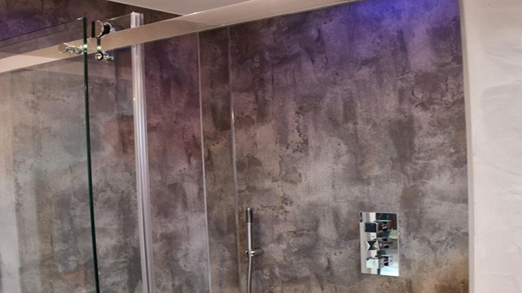 A modern bathroom with a glass shower and stylish concrete walls. The ceiling lighting creates a pleasant atmosphere.