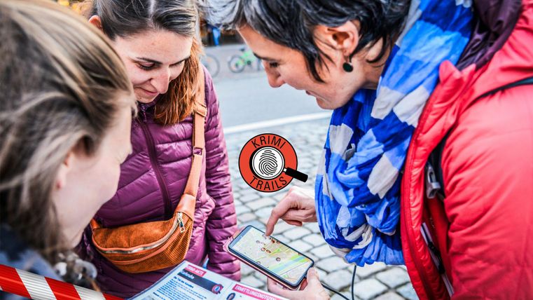 Trois femmes regardent un smartphone et discutent ensemble. En arrière-plan, on peut voir des vues urbaines qui montrent l'environnement urbain.