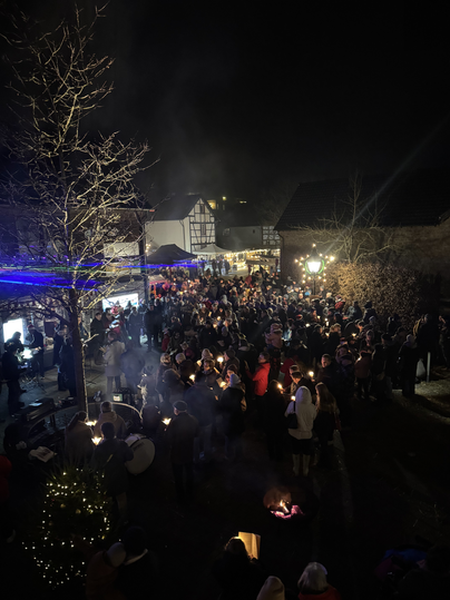 Eine große Menschenmenge versammelt sich bei einer Veranstaltung am Abend. Lichter und Rauch schaffen eine festliche Atmosphäre.