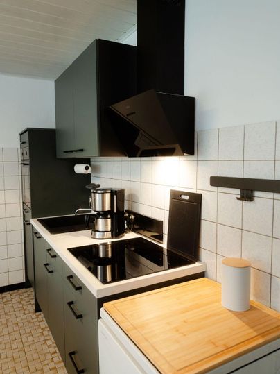 Une cuisine moderne avec des armoires noires laquées et un design clair et simple. La surface de cuisson est bien équipée et il y a un plan de travail en bois.