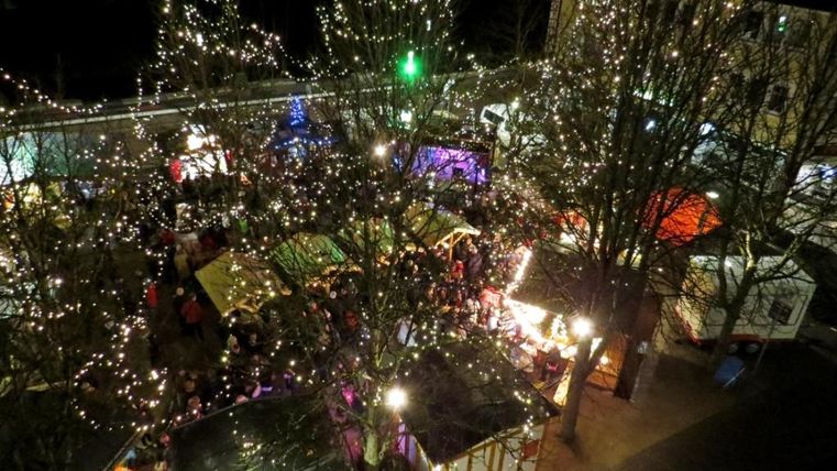 Een feestelijke kerstmarkt met veel lichtjes en versierde kraampjes. Mensen genieten van de sfeer en de feestelijke stemming.