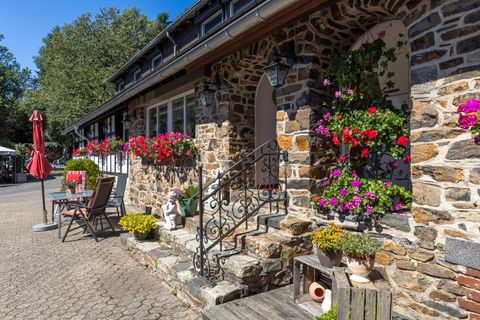 Une maison accueillante avec une façade en pierre et des pots de fleurs colorés. Devant la maison, il y a des chaises et un parasol.