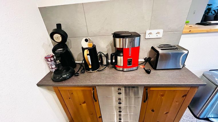 Een moderne keuken met verschillende elektrische apparaten, waaronder een koffiezetapparaat, een waterkoker, een toaster en een keukenhulp. De ruimte is licht en vriendelijk ingericht.